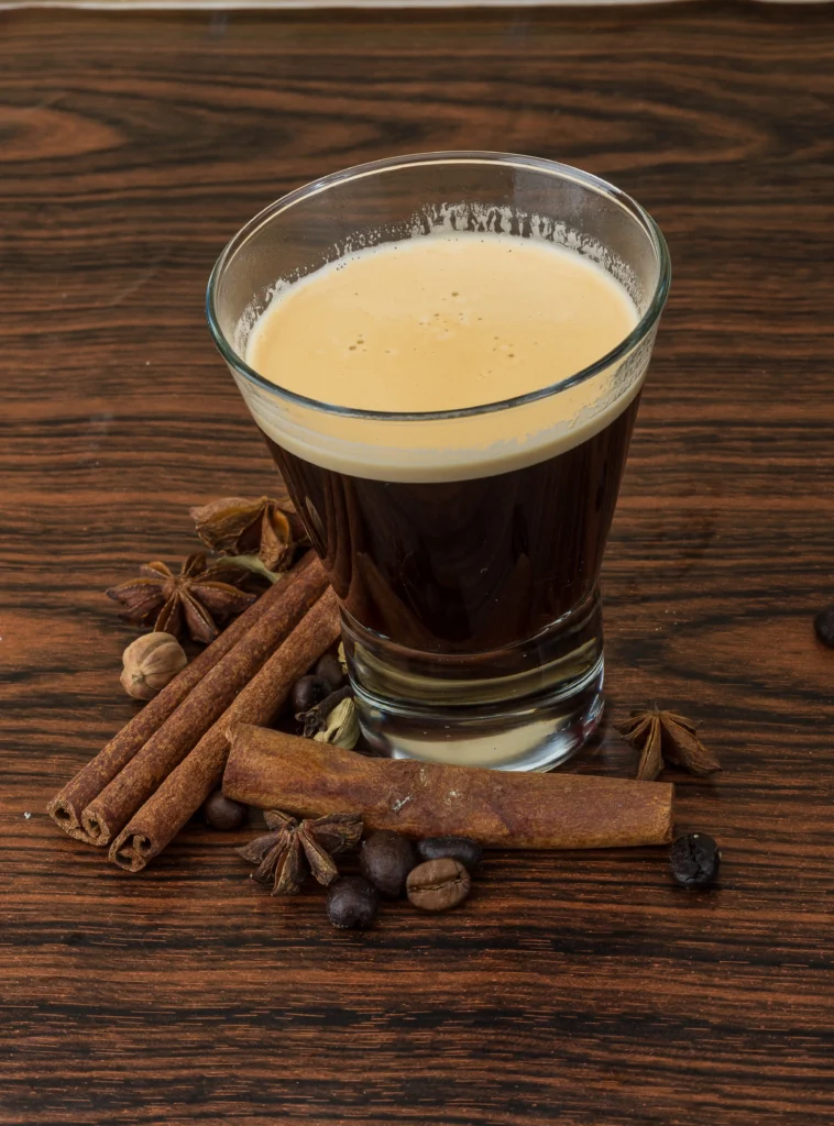 A steaming cup of Café de Olla served in a traditional clay mug, surrounded by cinnamon sticks, piloncillo, and coffee beans on a rustic wooden table.