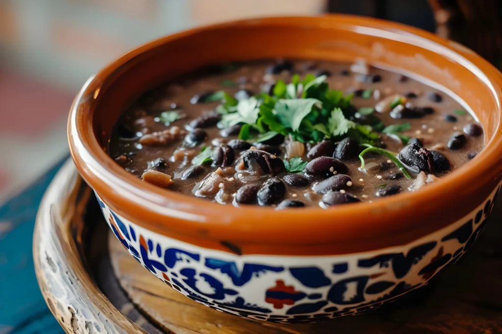 Close-up of a bowl of Chipotle Black Beans garnished with fresh cilantro and lime wedges, showcasing their bold, smoky texture